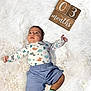 baby, blue_shorts, child, curious_expression, cute, decor, dinosaur_pajamas, fluffy_rug, indoors, infant, lying_down, milestone, months_marker, newborn, portrait, small_hands, socks, soft_texture, white_background, wooden_blocks