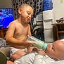 Theodore is registered to the contest to win money with this photo: baby, toddler, feeding, bottle, diaper, indoor, living_room, child, cute, care, toy, television, curtains, water_dispenser, furniture, blanket, car_seat, person, smiling, family
