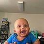 Theodore is registered to the contest to win money with this photo: baby, blue_onesie, smile, hands, indoor, living_room, bookshelf, books, furniture, person, child, happy, face, infant, holding, expression, home, seacreatures, clothing, background