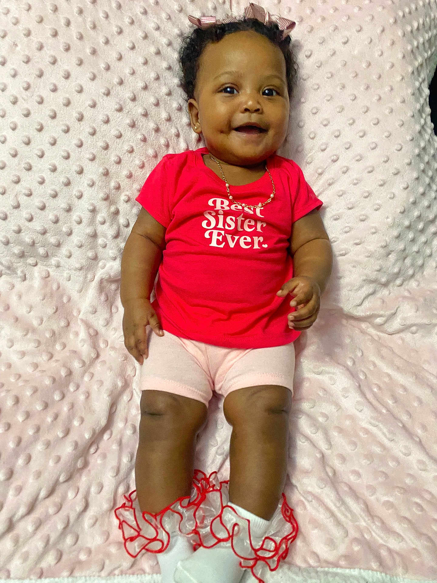 Kaliyah is registered to the contest to win money with this photo: baby, infant, child, smiling, pink_blanket, red_shirt, best_sister_text, cute, portrait, gold_necklace, hair_bow, socks, ruffle_socks, legs, hands, dimples, eyes, cheeks, blanket_texture, lying_down