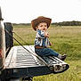 child, toddler, cowboy_hat, jeans, belt, boots, truck, tailgate, field, grass, outdoor, smile, pointing, portrait, daylight, hat, western, boy, cute, nature