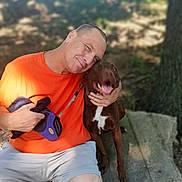 Starberry Hemberger is registered to the contest to win money with this photo: affection, canine, dog, grass, happy, human, leash, man, nature, orange_shirt, outdoor, park, pet, shoes, shorts, sitting, smile, stone, sunlight, tree