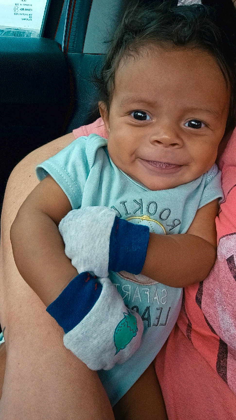 arm, baby, car_interior, casual, child, closeup, clothing, curly_hair, cute, happy, holding, infant, mittens, onesie, person, portrait, seat, skin, smiling, young