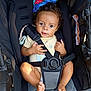 Grayson is registered to the contest to win money with this photo: baby, child, stroller, safety_harness, toy, frog_toy, curly_hair, clothing, foot, hand, seat, black, blue, red, green, yellow, infant, cute, portrait, indoor