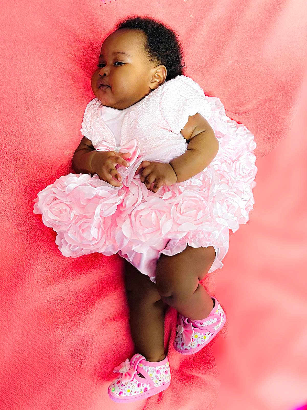 Amina is registered to the contest to win money with this photo: baby, infant, pink_dress, soft_blanket, cute, child, footwear, shoes, curly_hair, chubby_cheeks, laying_down, adorable, portrait, indoor, one_person, young_child, fashion, soft_texture, pretty, resting