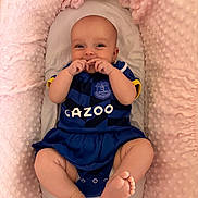 Annie joined the competition — help win amazing prizes! baby, infant, smiling, blue_clothing, football_jersey, everton, cushion, pink_blanket, soft_texture, cute, happy, lying_down, small_feet, hands_near_mouth, indoor, cozy, child, portrait, playful, comfortable