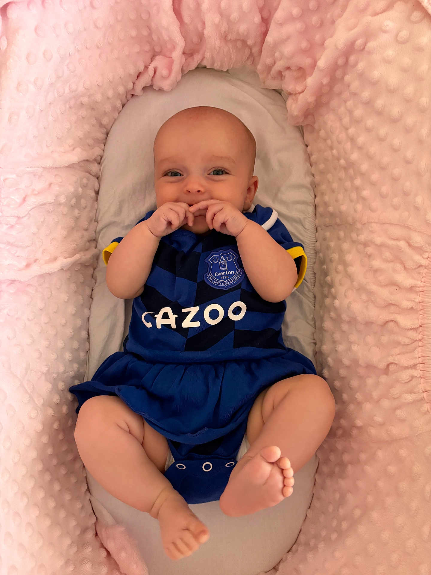 Annie joined the competition — help win amazing prizes! baby, infant, smiling, blue_clothing, football_jersey, everton, cushion, pink_blanket, soft_texture, cute, happy, lying_down, small_feet, hands_near_mouth, indoor, cozy, child, portrait, playful, comfortable