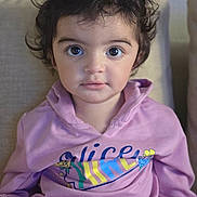 Haya is registered to the contest to win money with this photo: child, toddler, curly_hair, purple_hoodie, sitting, couch, indoor, face, large_eyes, portrait, clothing, person, young_child, casual, expression, comfortable, home, cute, looking_at_camera, cozy