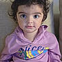 child, toddler, curly_hair, purple_hoodie, sitting, couch, indoor, face, large_eyes, portrait, clothing, person, young_child, casual, expression, comfortable, home, cute, looking_at_camera, cozy