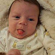 Kylo is registered to the contest to win money with this photo: baby, infant, tongue_out, blanket, cozy, cute, face, clothing, sleepwear, soft_texture, hand, portrait, young_child, indoors, expression, playful, skin, head, person, wrapped