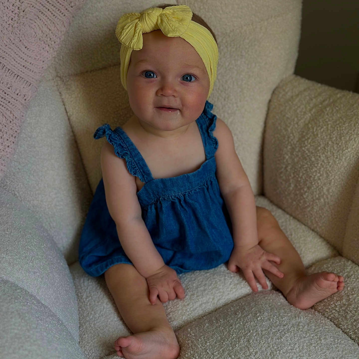 Kalani is registered to the contest to win money with this photo: baby, barefoot, blue_eyes, child, comfortable, cozy_chair, cute, denim_romper, happy, headwear, indoors, infant, portrait, sitting, small_hands, smiling, soft_lighting, textured_fabric, yellow_headband, young