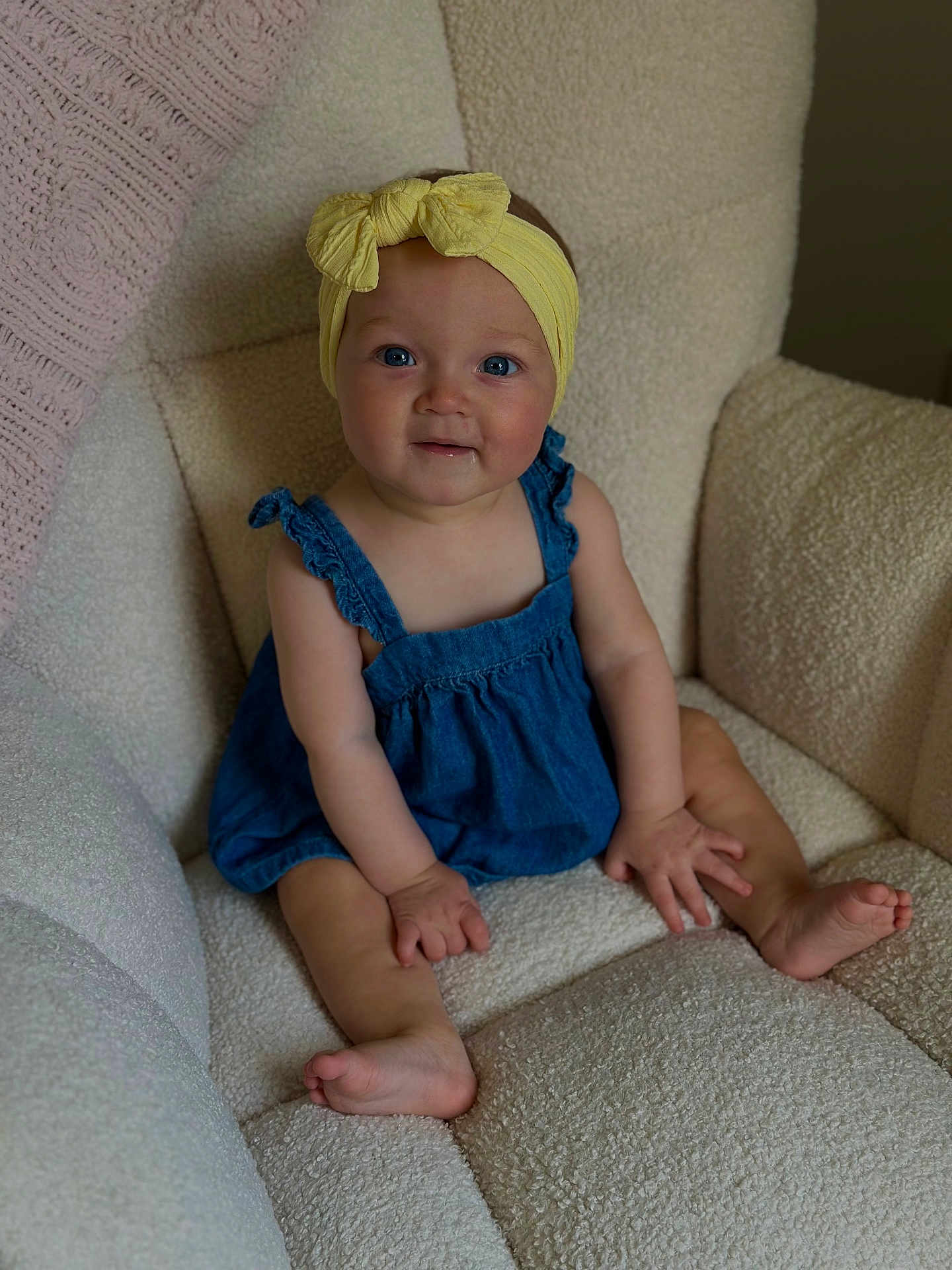 Kalani is registered to the contest to win money with this photo: baby, child, blue_eyes, yellow_headband, denim_romper, sitting, cozy_chair, textured_fabric, indoors, cute, smiling, barefoot, small_hands, portrait, infant, comfortable, soft_lighting, happy, young, headwear