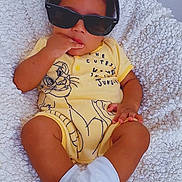Kaobichukwuha is registered to the contest to win money with this photo: baby, child, sunglasses, yellow_onesie, white_socks, blanket, infant, cute, indoor, portrait, smiling, baby_clothes, soft_texture, plush, relaxed, fashion, toddler, person, cozy, toy