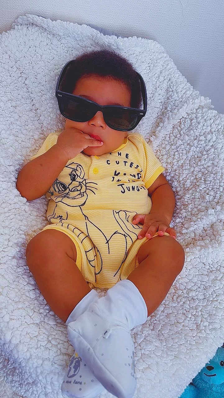 Kaobichukwuha is registered to the contest to win money with this photo: baby, child, sunglasses, yellow_onesie, white_socks, blanket, infant, cute, indoor, portrait, smiling, baby_clothes, soft_texture, plush, relaxed, fashion, toddler, person, cozy, toy