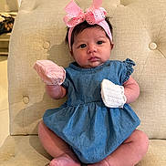 Leilani is registered to the contest to win money with this photo: baby, infant, child, blue_dress, pink_bow, headband, mittens, sitting, beige_chair, cushion, indoors, cute, portrait, young_child, face, feet, hands, expression, soft_lighting, furniture