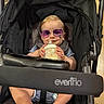 Weston joined the competition — help win amazing prizes! baby, sunglasses, stroller, milk_bottle, infant, child, smile, person, clothing, footwear, seat, black_fabric, purple, cute, cheerful, indoor, baby_bottle, holding, legs, head