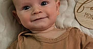 Weston joined the competition — help win amazing prizes! baby, infant, smiling, face, portrait, clothing, brown_shirt, quilted_blanket, lying_down, cute, young_child, happy, indoors, human, child, head, skin, eyes, hand, expression