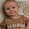 baby, infant, smiling, face, portrait, clothing, brown_shirt, quilted_blanket, lying_down, cute, young_child, happy, indoors, human, child, head, skin, eyes, hand, expression