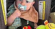 Weston is registered to the contest to win money with this photo: baby, bib, blue_eyes, cap, car_interior, car_seat, casual_clothing, checkered_shirt, child, colorful, cute, indoor, infant, pacifier, plush_toy, seatbelt, sitting, soft_toy, toy, young_child