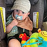 baby, child, car_seat, pacifier, cap, plush_toy, blue_eyes, bib, checkered_shirt, seatbelt, indoor, cute, infant, toy, colorful, soft_toy, young_child, sitting, casual_clothing, car_interior