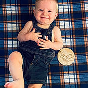 Weston joined the competition — help win amazing prizes! baby, infant, smiling, overalls, plaid_blanket, blue, orange, wooden_sign, eight_months, child, cute, portrait, lying_down, happy, barefoot, skin, one_leg_raised, indoor, young_child, clothing