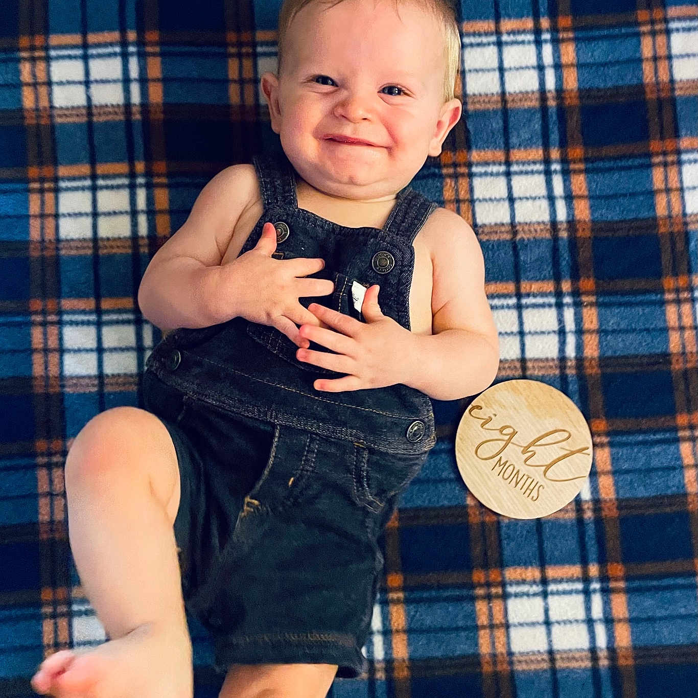 Weston joined the competition — help win amazing prizes! baby, infant, smiling, overalls, plaid_blanket, blue, orange, wooden_sign, eight_months, child, cute, portrait, lying_down, happy, barefoot, skin, one_leg_raised, indoor, young_child, clothing