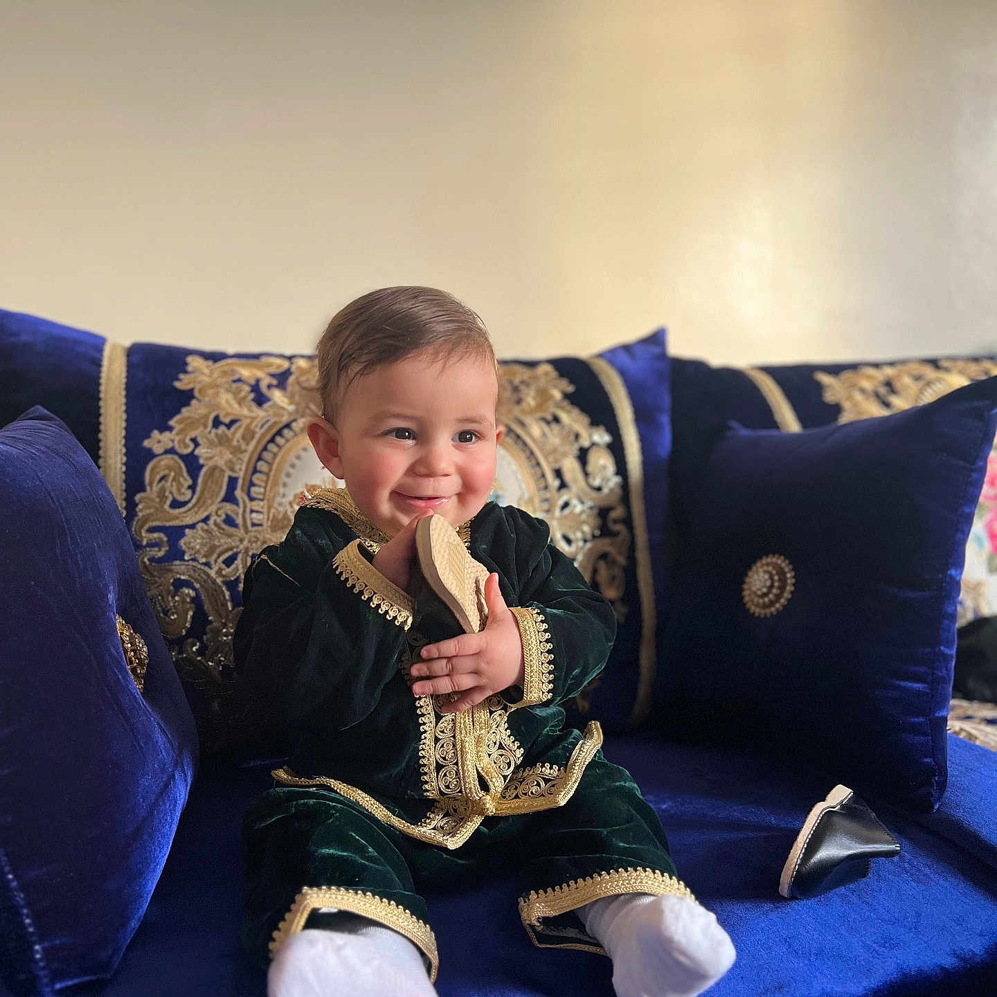 Amir a rejoint le concours — aidez-le/la à gagner de superbes lots ! baby, child, smiling, couch, blue_cushion, embroidery, traditional_clothing, indoor, plush_furniture, shoe, white_socks, happy, portrait, seated, decorative_pillow, luxury, soft_lighting, cute, infant, handheld_object