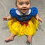 baby, child, smiling, dress, costume, snow_white, yellow_skirt, blue_top, red_bow, barefoot, sitting, floor, portrait, cute, happy, indoor, person, face, young, toddler