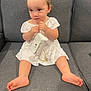 barefoot, casual, child, couch, curly_buns, curly_hair, cute, expression, furniture, gold_chain, gray_couch, indoor, portrait, purse, sitting, small_purse, soft_lighting, toddler, white_dress, young_child