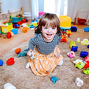 Rhielly is registered to the contest to win money with this photo: child, toddler, smiling, striped_shirt, orange_skirt, toys, carpet, indoor, play, happy, person, cute, young, kid, room, colorful, fun, joy, playful, bright