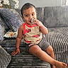 toddler, child, sitting, sofa, couch, smiling, portrait, indoor, living_room, snack, food, hand, pajamas, car_pattern, gray, cushion, flowers, radiator, cozy, photography
