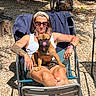 woman, dog, french_bulldog, outdoor, sunglasses, chair, tattoo, sunlight, relaxing, summer, pet, tongue_out, casual, headband, barefoot, gravel, arm_chair, jewelry, shorts, tank_top