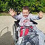 child, wheelchair, blanket, smiling, outdoor, greenery, sunlight, person, happy, hoodie, nature, park, hands, young, casual_clothing, sitting, accessibility, wheel, shadow, joyful