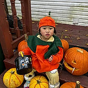 Khai My joined the competition — help win amazing prizes! child, toddler, pumpkin_costume, halloween, pumpkins, bucket, orange, green, wooden_steps, fall, festive, cute, outdoor, seasonal, costume, decorations, playful, expression, clothing, holiday