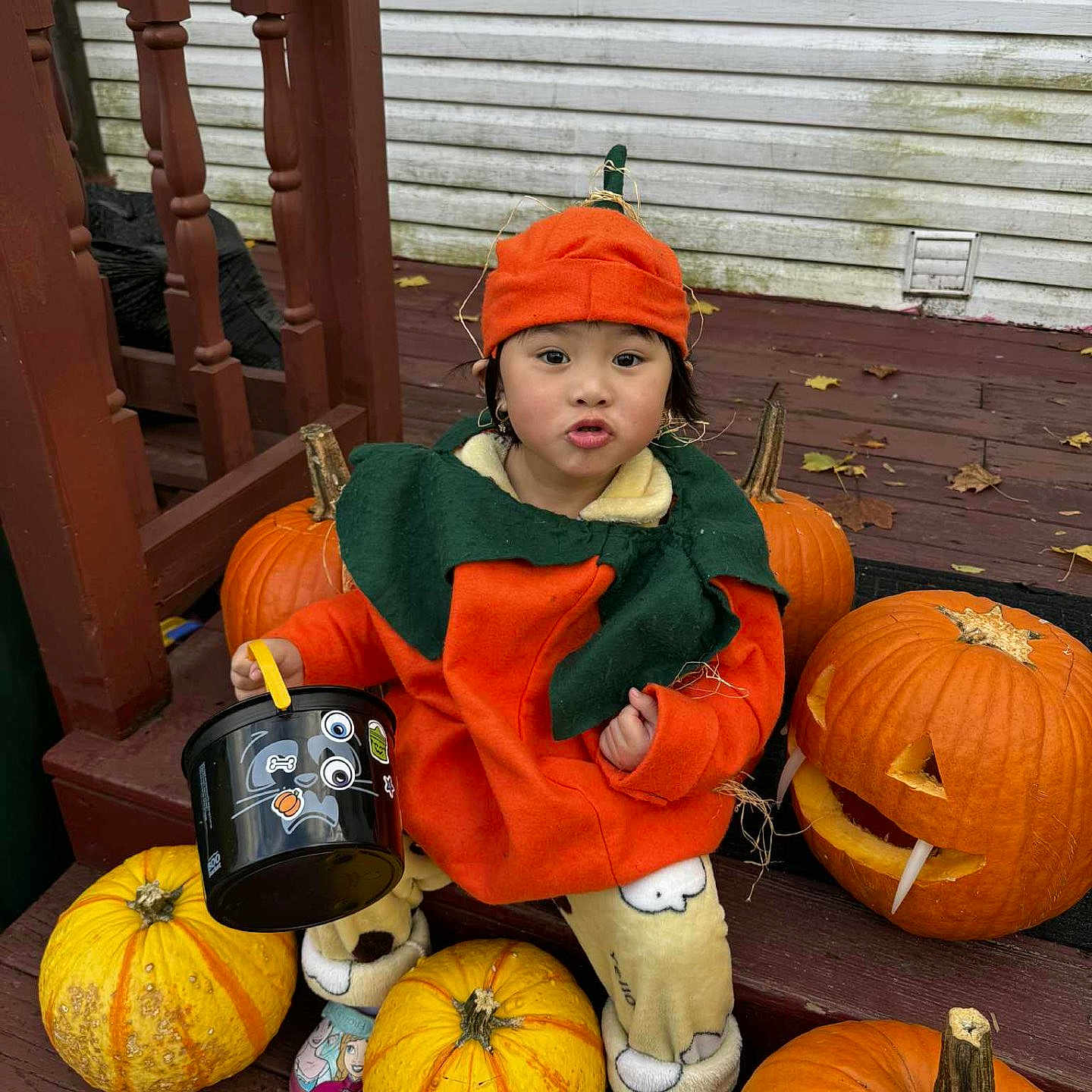 Khai My joined the competition — help win amazing prizes! bucket, child, clothing, costume, cute, decorations, expression, fall, festive, green, halloween, holiday, orange, outdoor, playful, pumpkin_costume, pumpkins, seasonal, toddler, wooden_steps