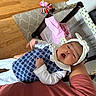 Ailany is registered to the contest to win money with this photo: newborn, baby, infant, yawning, sleepy, headband, bow, blue_outfit, white_clothing, knitwear, lap, adult, playpen, baby_gear, toys, stuffed_animal, rug, hardwood_floor, indoor, portrait