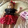 baby, infant, pacifier, headband, red_bow, polka_dot_skirt, black_top, bed, blanket, pillow, milestone_sign, 2_months, cartoon_cat, clothing, person, cute, lying_down, soft_toys, indoor, happy