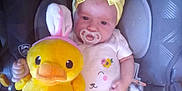 Aurora joined the competition — help win amazing prizes! baby, car_seat, child, child_seat, comfort, cute, face, indoor, infant, pacifier, person, plush_toy, sitting, smile, soft_toy, stuffed_animal, toy, white_socks, yellow_headband, yellow_pants