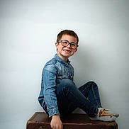 Leo participe au concours pour gagner de l'argent avec cette photo : child, boy, glasses, denim_shirt, jeans, socks, sitting, vintage_suitcase, smile, portrait, indoor, casual, happy, young, fashion, studio, kid, person, isolated, background