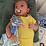 baby, pacifier, plush_toy, yellow_clothing, bed, pillow, blanket, infant, child, cute, sleepwear, soft_toy, relaxing, indoors, resting, hand, face, head, lying_down, expression