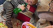 Rodger is registered to the contest to win money with this photo: child, toddler, pajamas, striped_clothing, couch, pillows, hot_dog, ketchup, cheese, plate, bottle, window, rug, penguin_pattern, snowflake_pattern, indoor, smiling, food, person, tattoo