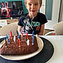 child, boy, birthday_cake, candles, smoke, table, plate, indoor, television, chair, tshirt, celebration, home, food, happy, smiling, cake, furniture, person, event