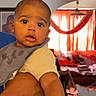 Isaiah is registered to the contest to win money with this photo: baby, child, person, indoor, living_room, curtains, arm, holding, expression, face, clothing, bib, furniture, couch, window, light, home, portrait, skin, head