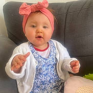 Ambre participe au concours pour gagner de l'argent avec cette photo : baby, bow, cardigan, child, couch, curious, cushion, cute, floral_dress, gray_couch, headband, indoor, person, pink, portrait, reaching_out, seated, soft_toys, white_clothing, young_child