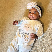 Naïma a rejoint le concours — aidez-le/la à gagner de superbes lots ! baby, infant, girl, headband, flower, onesie, white_clothing, carpet, floor, lying_down, cute, child, portrait, soft_texture, indoors, small_hands, expression, adorable, star_pattern, cozy