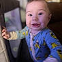 baby, child, onesie, blue_clothing, banana_pattern, playpen, indoor, face, smile, happy, young_child, closeup, person, human, cute, expression, hand, head, infant, portrait