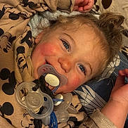 Mylan a rejoint le concours — aidez-le/la à gagner de superbes lots ! child, toddler, baby, pacifier, pacifiers, smile, blue_eyes, rosy_cheeks, blanket, mickey_mouse_print, pajamas, bed, stuffed_animal, hair_bun, hand, closeup, portrait, cozy, playful, interior