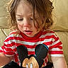 candid, casual_clothing, child, close_up, concentration, couch, curly_hair, eyelashes, indoor, lips, messy_hair, mickey_mouse, pale_skin, portrait, red_stripes, rosy_cheeks, sitting, soft_light, t_shirt, toddler