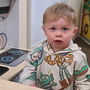 Colton joined the competition — help win amazing prizes! child, toddler, hoodie, toy_story, play_kitchen, indoor, blond_hair, blue_eyes, curious, standing, clothing, face, young_child, appliance, pretend_play, furniture, person, casual_wear, light_skin, expression