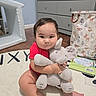 Nicholas joined the competition — help win amazing prizes! baby, infant, child, portrait, sitting, hugging, stuffed_animal, elephant, toy, red_shirt, smiling, serious_expression, indoor, playroom, nursery, dresser, rug, storybook, basket, home